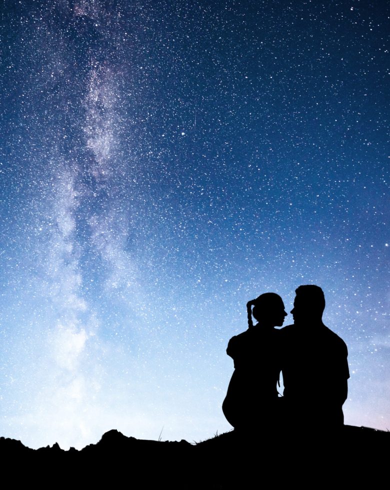 Milky Way with silhouette of people. Landscape with night starry sky. Standing man and woman on the mountain with star light. Hugging couple against purple milky way. Beautiful galaxy. Universe.